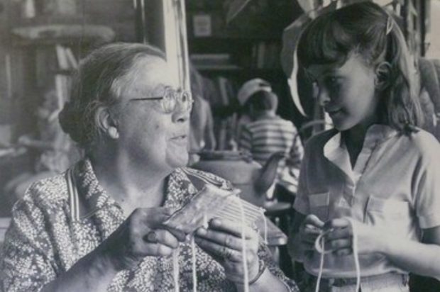 Photo noir et blanc d’une femme qui tisse avec une jeune fille sur un métier à tisser en carton.