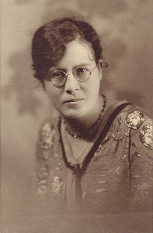 Portrait de studio sépia d’une jeune femme portant des lunettes.