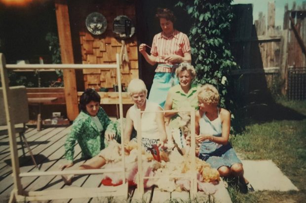 Photo couleur de cinq femmes sur une terrasse avec des piles de laine brute et deux métiers à tisser