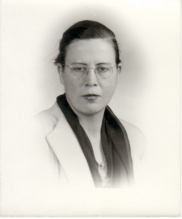 Portrait de studio en noir et blanc d’une jeune femme à lunettes, portant un foulard sombre et un blazer clair.