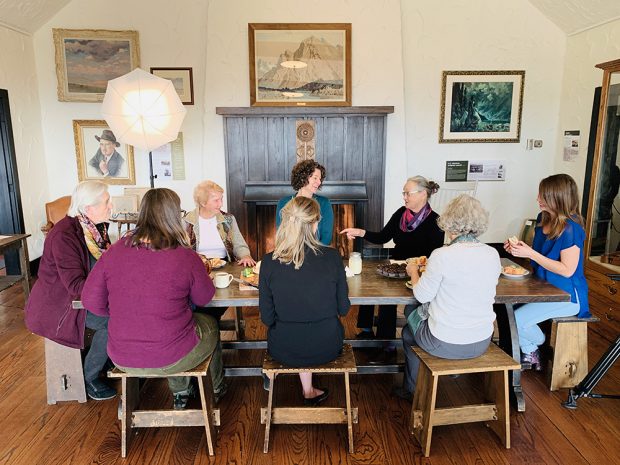 Photo couleur d’un groupe de femmes partageant un repas autour de la table; dessins sur les murs en arrière-plan.