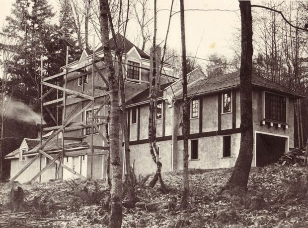 Photo noir et blanc d’une maison à colombages avec un échafaudage sur le côté et entourée d’arbres.