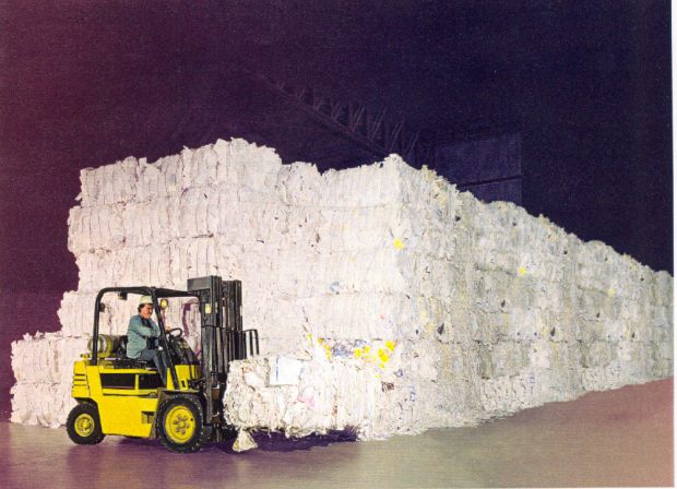 Photographie couleur d’un chariot élévateur devant plusieurs piles de ballots de retailles de papier. 