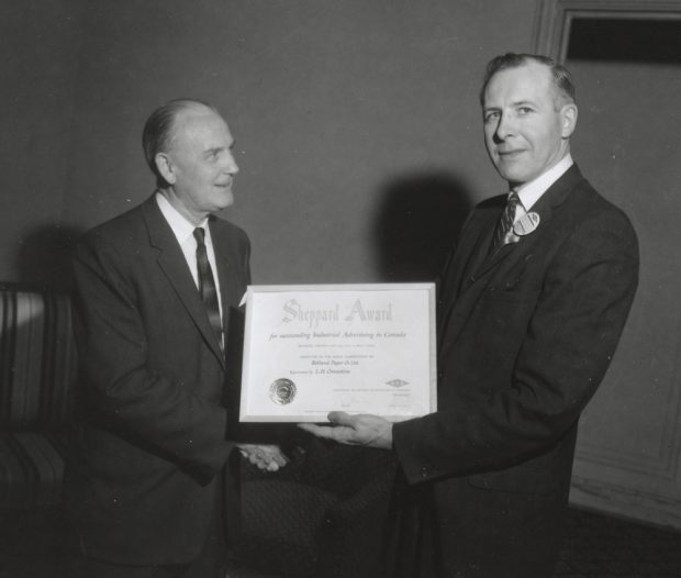Photographie noir et blanc d’un homme remettant un certificat à un autre homme pendant qu’ils se serrent la main.  
