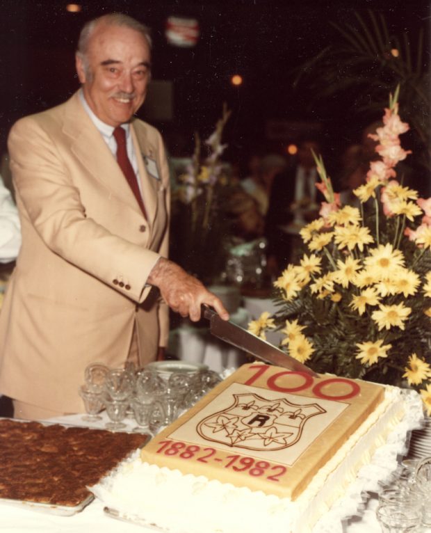 Photographie couleur d’un homme âgé s’apprêtant à couper un gâteau.   
