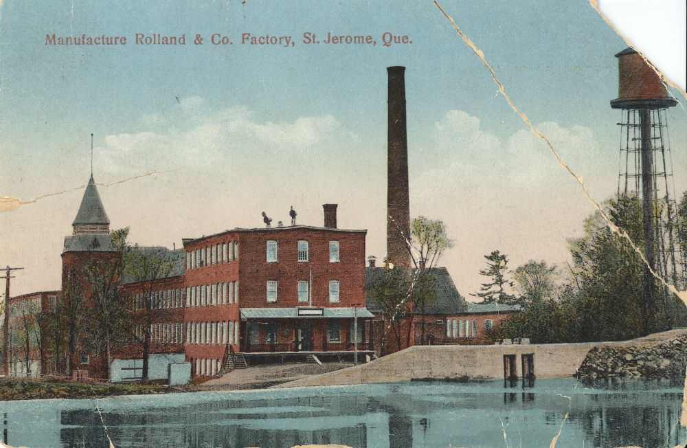 Image couleur de bâtiments près d’une grande cheminée et d’une rivière. 