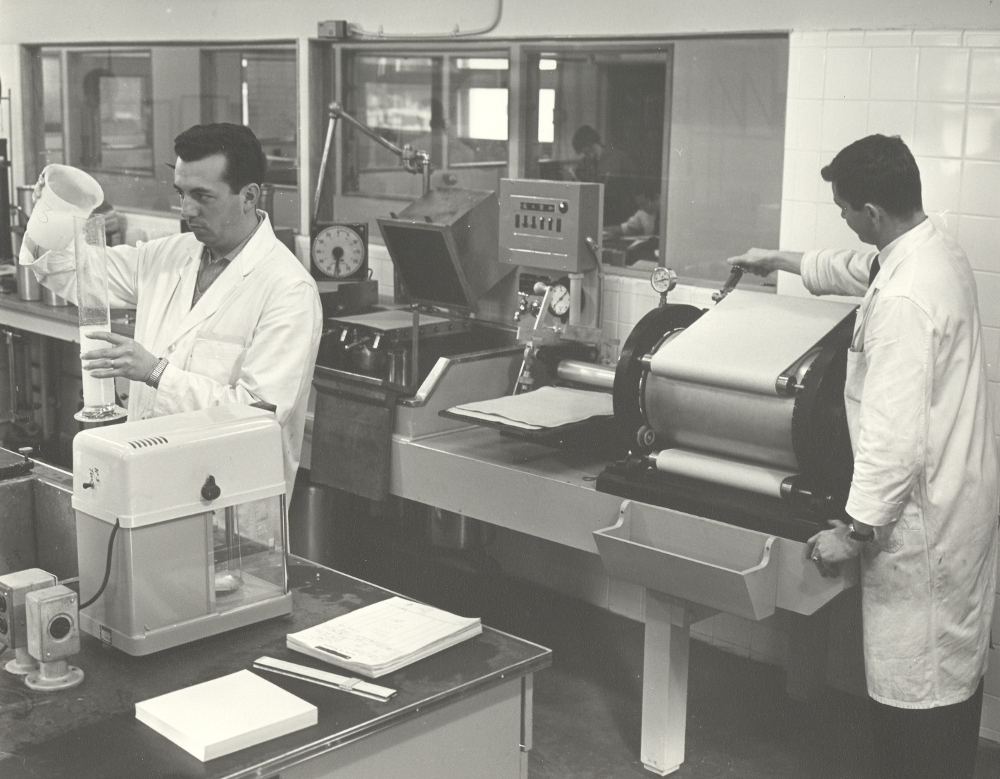 Photographie noir et blanc de deux hommes en sarrau blanc dans un laboratoire.