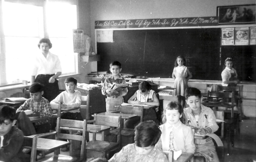 Photo en noir et blanc de la classe de Mme Golosky à l'école St. John's à la fin des années 1960. Les élèves sont assis sur des pupitres en bois face à l'avant, une jeune fille est représentée à l'arrière près d'un grand tableau noir.
