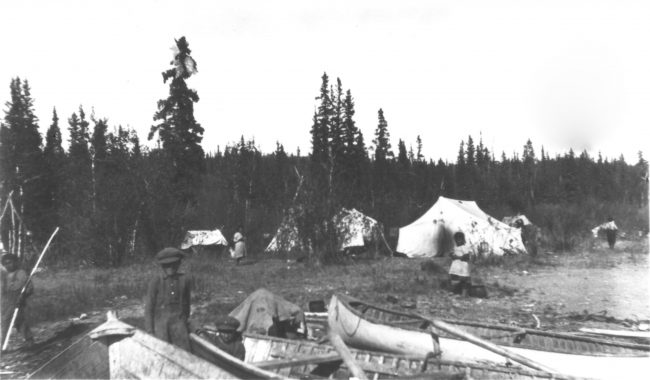 Une photo historique des années 1920 montre un camp installé avec plus de quatre tentes, des canoës posés le long de la rivière avec des enfants autour d'eux.