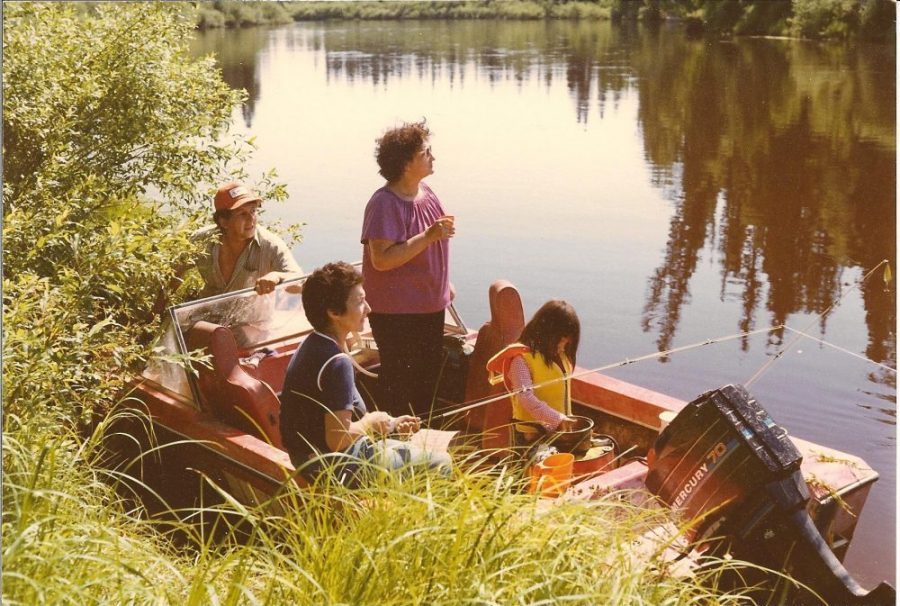 Une photo en couleur des années 1980 de personnes dans un bateau sur la rivière, les arbres de la forêt se reflétant dans l'eau.