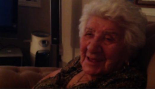 Photo en couleur d'une aînée, Elsie Yanik, assise dans un salon et chantant une berceuse crie.