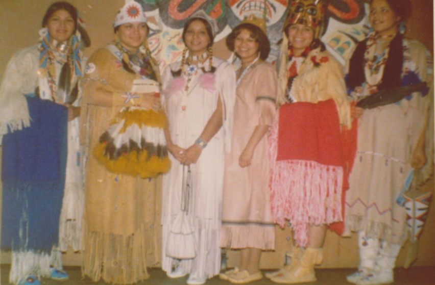 Six femmes vêtues de vêtements traditionnels sourient à la caméra.