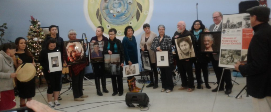 Des femmes et des hommes se tiennent ensemble devant un photographe, ils tiennent les portraits encadrés de dix femmes autochtones
