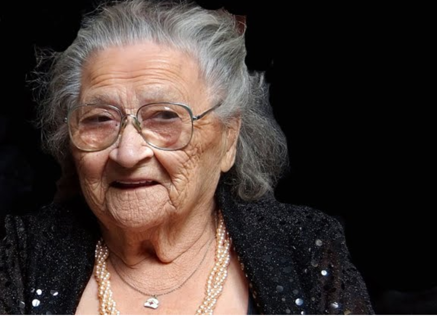 Portrait en couleur de Jenny Flett âgée portant un cardigan noir et des lunettes.