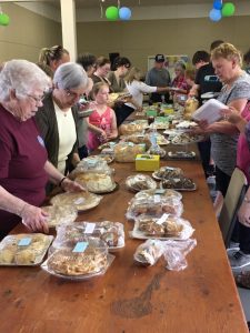 Pâtisseries exposées sur une table entourée de clients qui attendent le début de la vente à Monsktown