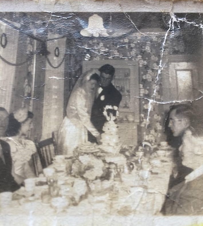 la mariée et le marié sont représentés en train de couper le gâteau de mariage au dîner de mariage d'Alice Drake à Oderin. les invités et les membres de la noce regardent