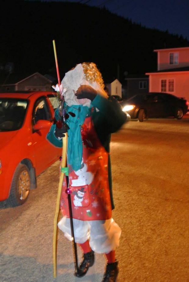 Un mummer marche dans la rue avec un bâton lors d’un défilé nocturne de mummers 