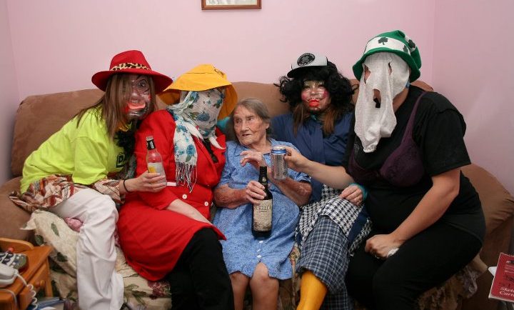 Quatre mummers prennent un verre de rhum assis avec une vieille dame sur un canapé plein à craquer