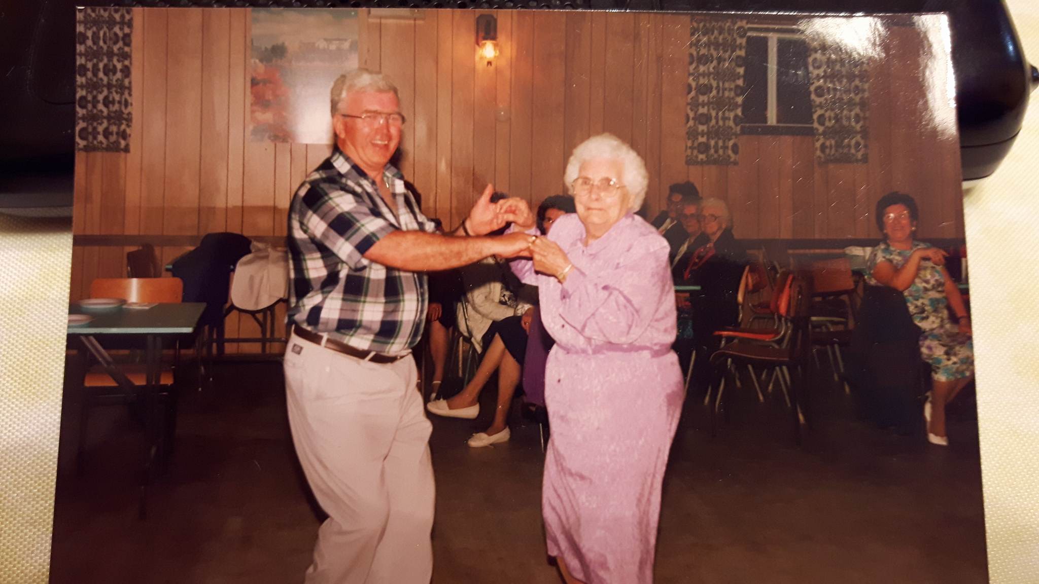 Un homme et une femme âgée en robe rose dansent dans une salle des fêtes