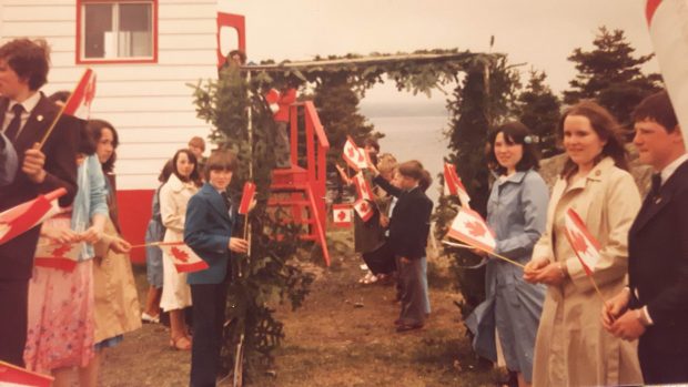 Des écoliers attendent l’arrivée de l’évêque debout sous une arche faite de branches de conifères.