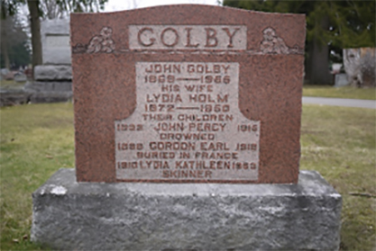 Une pierre tombale rectangulaire ornée au sommet portant le nom « GOLBY ».
