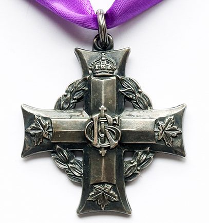 Une croix grecque accrochée à un ruban pourpre par un petit anneau. Une guirlande de laurier sous les bras de la croix. Un chiffre se trouve à l’intersection des deux bras. Une couronne surmonte le bras supérieur; trois feuilles d’érables se trouvent à l’extrémité des autres bras.