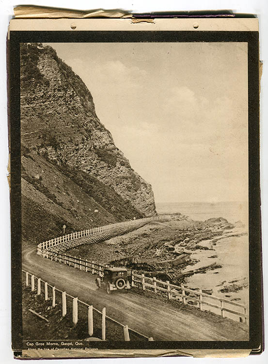 Photographie sépia d'une voiture circulant sur le Boulevard Perron, une route de gravier serpentant au pied d'un immense cap rocheux, passage étroit entre la falaise et la mer. Une simple barrière en bois sépare la route du rivage