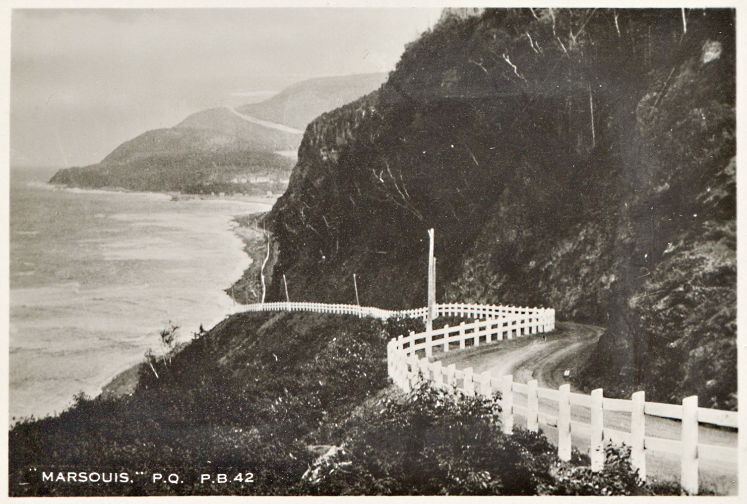 Photographie montrant le sinueux boulevard Perron dans la municipalité de Marsoui. Le boulevard Perron traverse en hauteur un cap rocheux et est bordé par une clôture de bois peint en blanc.