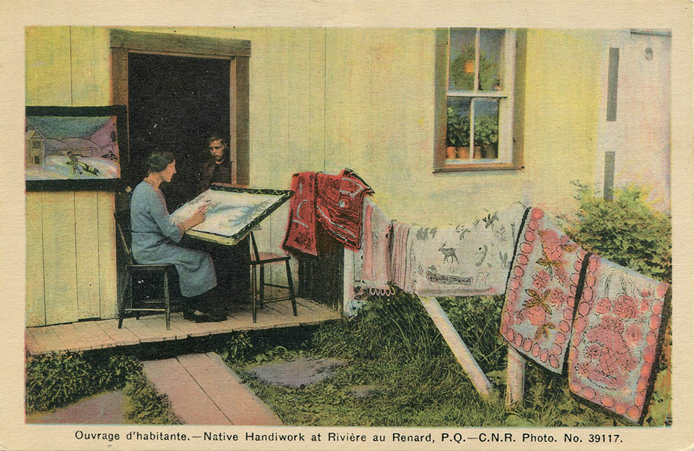 Carte postale. Photographie peinte à la main. Une femme est assise sur la galerie d’une maison. Elle brode une scène hivernale sur un tapis dont la base est posée sur ses genoux. Tout près d’elle, six tapis faits à la main sont déposés sur une clôture et un cadre, d’une scène hivernale, est accroché sur le mur extérieur de la maison. Dans l’ouverture de la porte ne jeune garçon observe sa mère broder. 