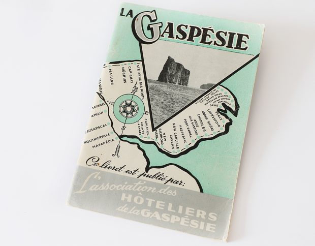 Page couverture d’un guide touristique. La Gaspésie a été tracée en noir et blanc sur un fonds vert pastel représentant le fleuve Saint-Laurent. Tous les villages qui se trouvent le long du tracé de la route 6 ont été identifiés. En entête, La Gaspésie est écrit en gros caractère. En dessous, de la photographie du Rocher Percé est présentée dans un encadré triangulaire. Au bas de la page il est écrit : Ce livret est publié pas L’association des hôteliers de la Gaspésie.