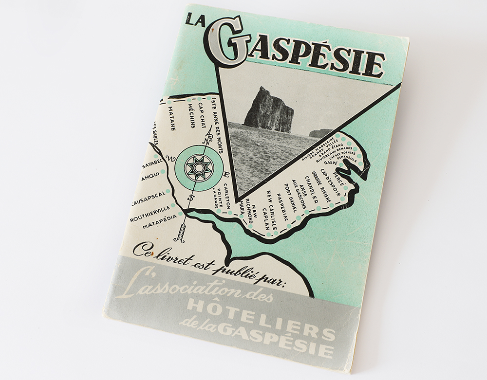 Page couverture d’un guide touristique. La Gaspésie a été tracée en noir et blanc sur un fonds vert pastel représentant le fleuve Saint-Laurent. Tous les villages qui se trouvent le long du tracé de la route 6 ont été identifiés. En entête, La Gaspésie est écrit en gros caractère. En dessous, de la photographie du Rocher Percé est présentée dans un encadré triangulaire. Au bas de la page il est écrit : Ce livret est publié pas L’association des hôteliers de la Gaspésie.