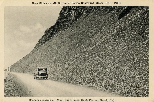 Photographie noir et blanc d’une voiture roulant sur le boulevard Perron. La route longe une pente abrupte tapissée de rochers plats, laissant l’impression d’un éboulement récent. 