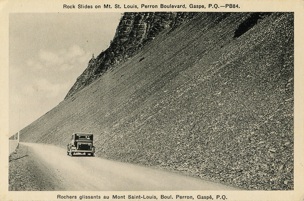 Photographie noir et blanc d’une voiture roulant sur le boulevard Perron. La route longe une pente abrupte tapissée de rochers plats, laissant l’impression d’un éboulement récent. 