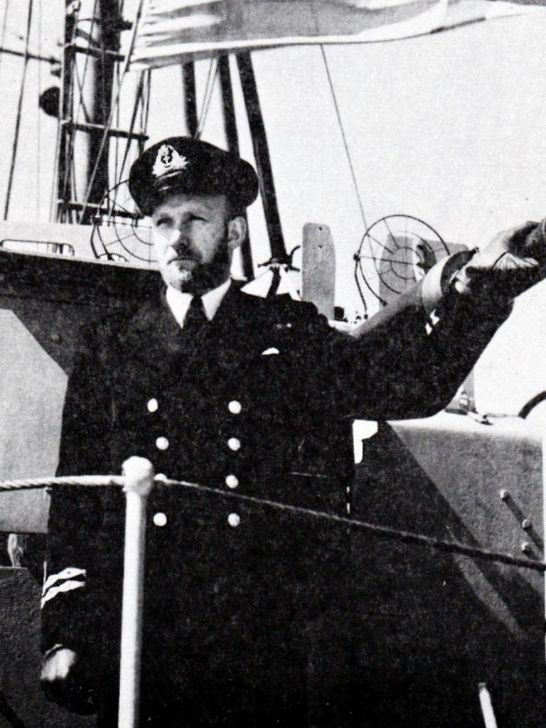 Un officier de la marine se tient à côté d’un canon de pont sur un navire de guerre.