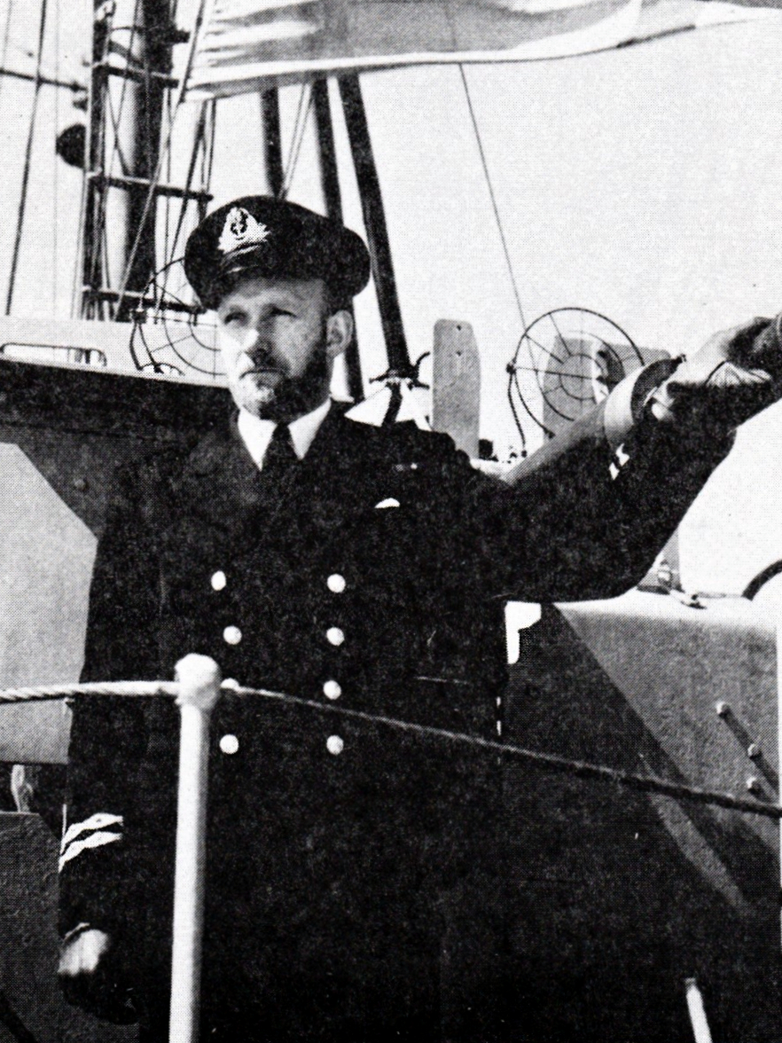 Un officier de la marine se tient à côté d’un canon de pont sur un navire de guerre.