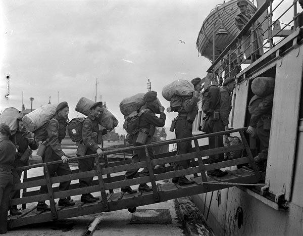 Des soldats transportant des sacs de voyage embarquent sur un navire.