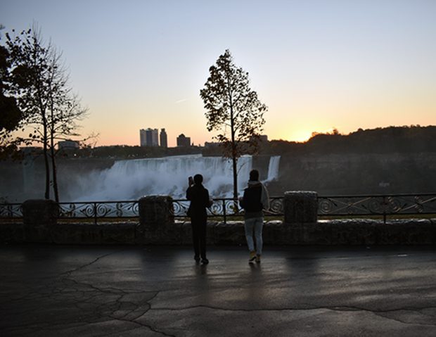 Deux chercheurs se tiennent près d’une rambarde au lever du soleil, face aux chutes du Niagara enveloppées de brume