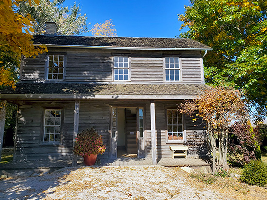 La maison de Josiah Henson, une demeure en bois à deux étages avec un parement vieilli et un porche couvert. Cette résidence historique fait partie du Musée Josiah Henson de l’histoire des Afro-Canadiens, situé à Dresden, en Ontario, et est entourée d’arbres aux couleurs d’automne.