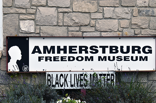 Gros plan sur le panneau d’entrée du Musée de la liberté d’Amherstburg, fixé à un mur de pierre, avec un plus petit panneau « Black Lives Matter » placé en dessous. Photo d’Alex Allasra.
