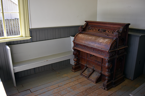 L’orgue original de l’église située dans la Pioneer Church au Musée Josiah Henson de l’histoire afro-canadienne. L’orgue en bois orné est placé dans un coin, à côté de bancs simples et de murs peints. Photo de Blessing Ogunyemi.