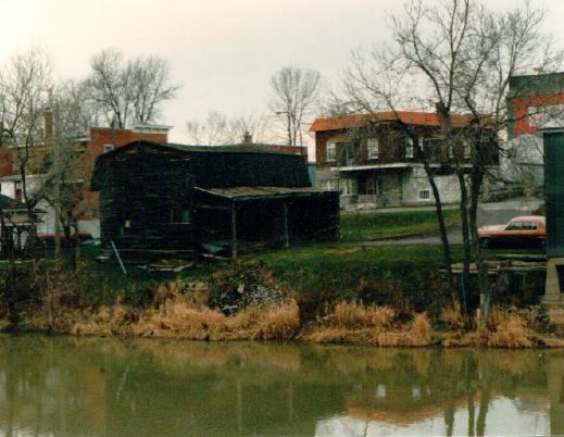 Plan large d’un bâtiment en bois noirci et usé sur le bord d’une rivière.	