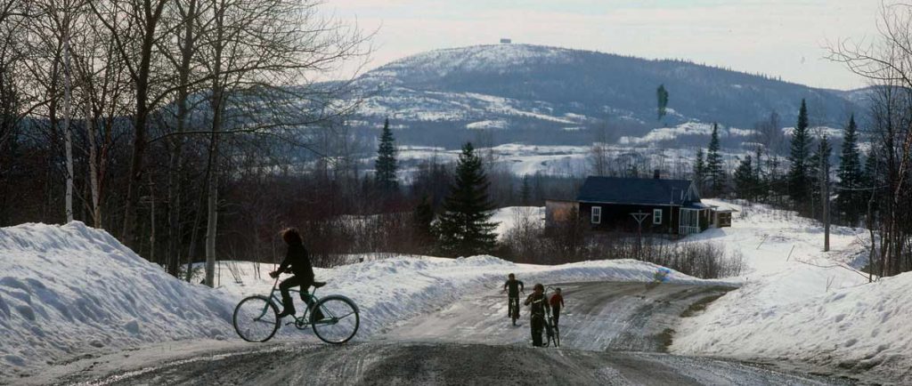 Vue d'un paysage et d'une route rurale au printemps durant la fonte des neiges. Des enfants circulent à vélo.