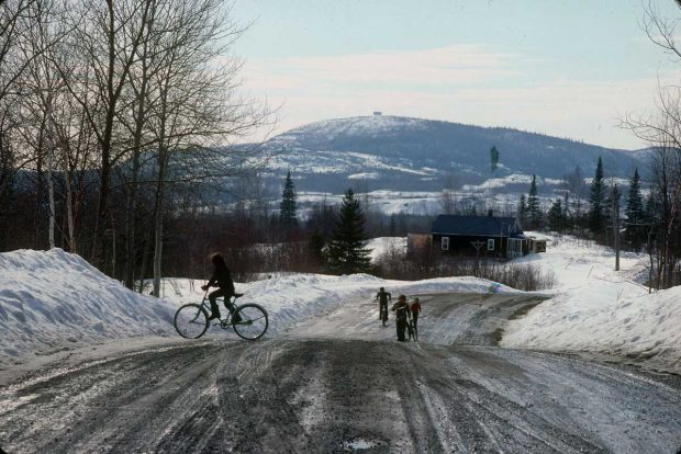 Vue d'un paysage et d'une route rurale au printemps durant la fonte des neiges. Des enfants circulent à vélo.