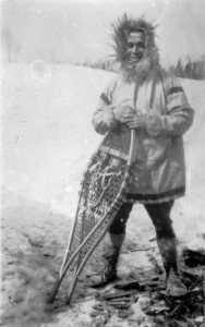 Photographie noir et blanc d'un homme en parka qui tient une paire de raquettes, en hiver, à l’extérieur.