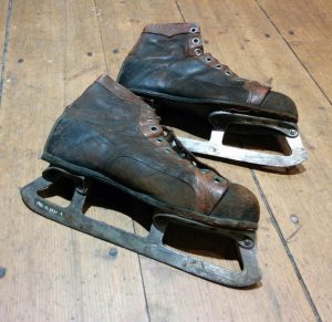 Photographie couleur d’une paire de patins à glace de couleur brune et noire, au cuir défraîchi.