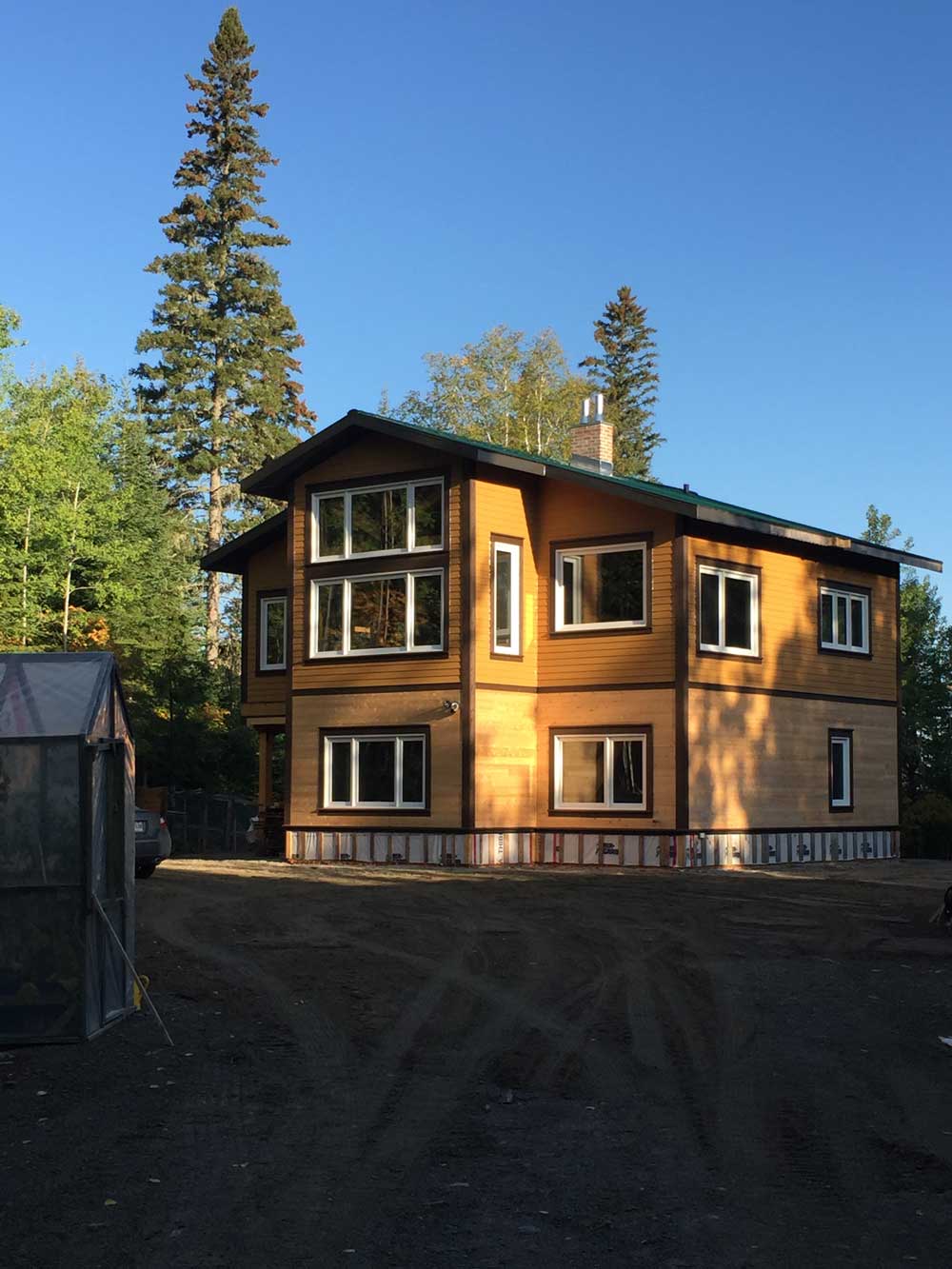 Vue sur une maison nouvellement construite, à deux étages, entourée d'arbres.