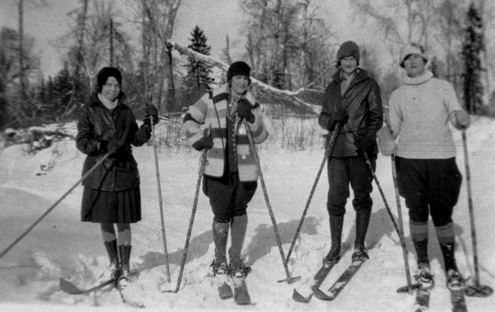 Photographie noir et blanc de quatre femmes en ski de fond, l’hiver, en forêt.