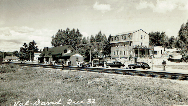 Carte postale montrant l’Auberge La belle Chaumière à Val-David, la voie ferrée, la gare de Val-David et de vieilles voitures des années 1940.