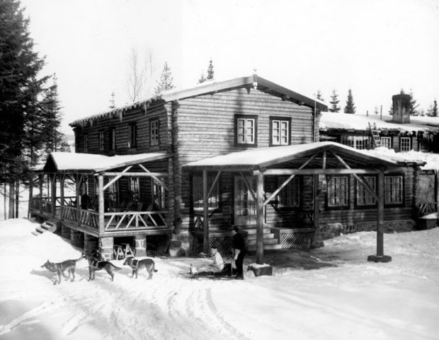 L’Auberge La Sapinière, en noir et blanc, à l’hiver 1937; édifice de bois rond avec un traîneau à chien en façade.