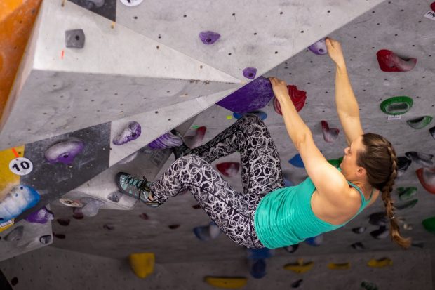 Jeune femme utilisant ses mains et ses pieds afin de rester accroché à des prises ressemblant à des poignées sur un mur artificiel. 